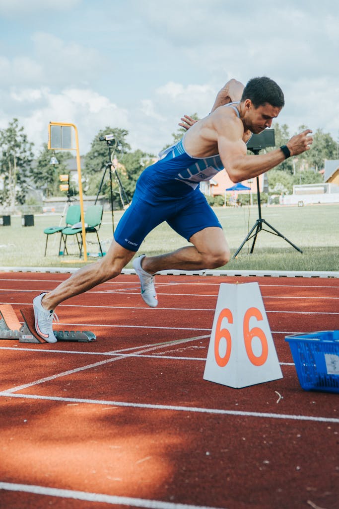 A determined male athlete sprints from starting blocks on an outdoor track.
