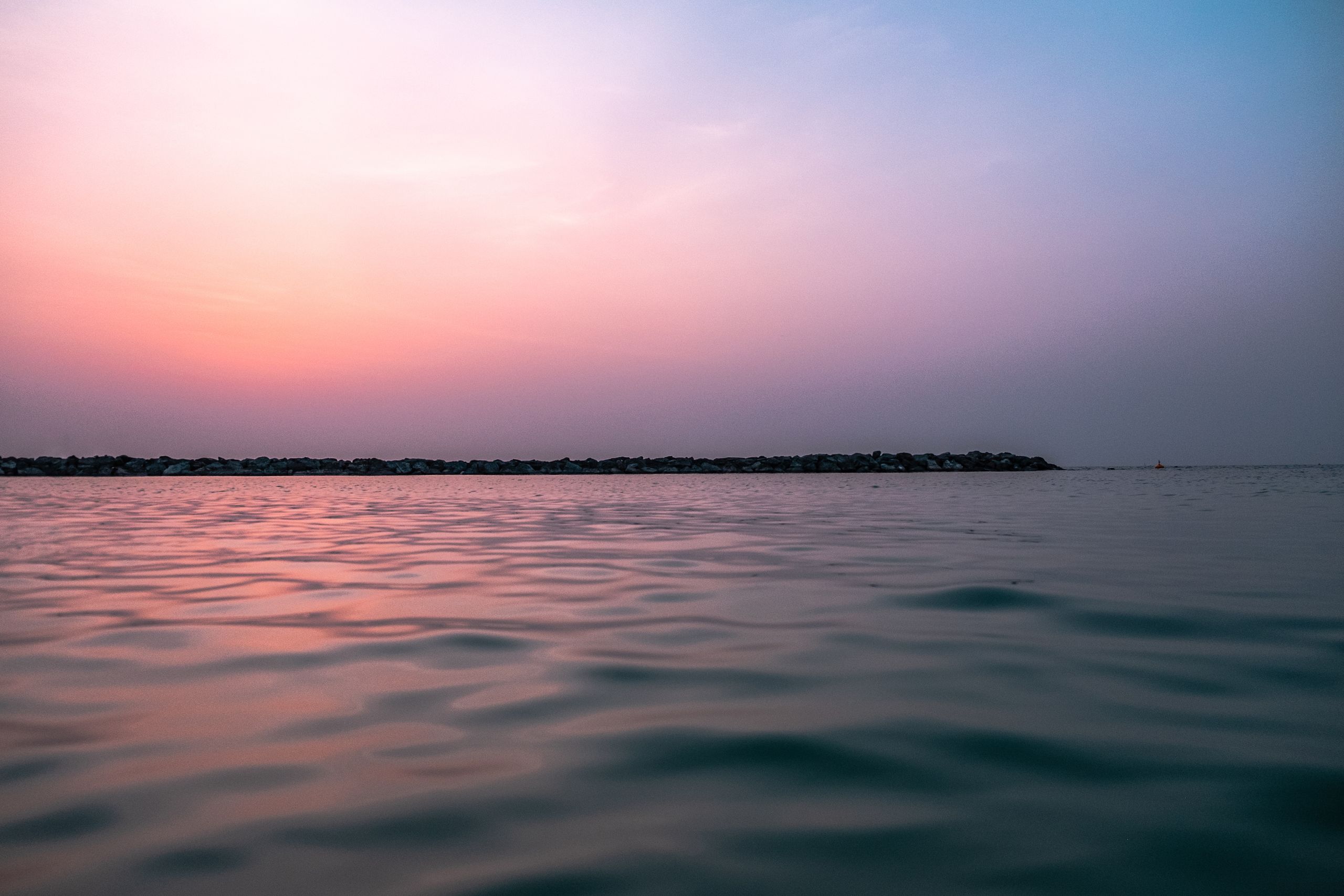 Peaceful view of the ocean at sunset with soft pastel skies, perfect for relaxing themes.