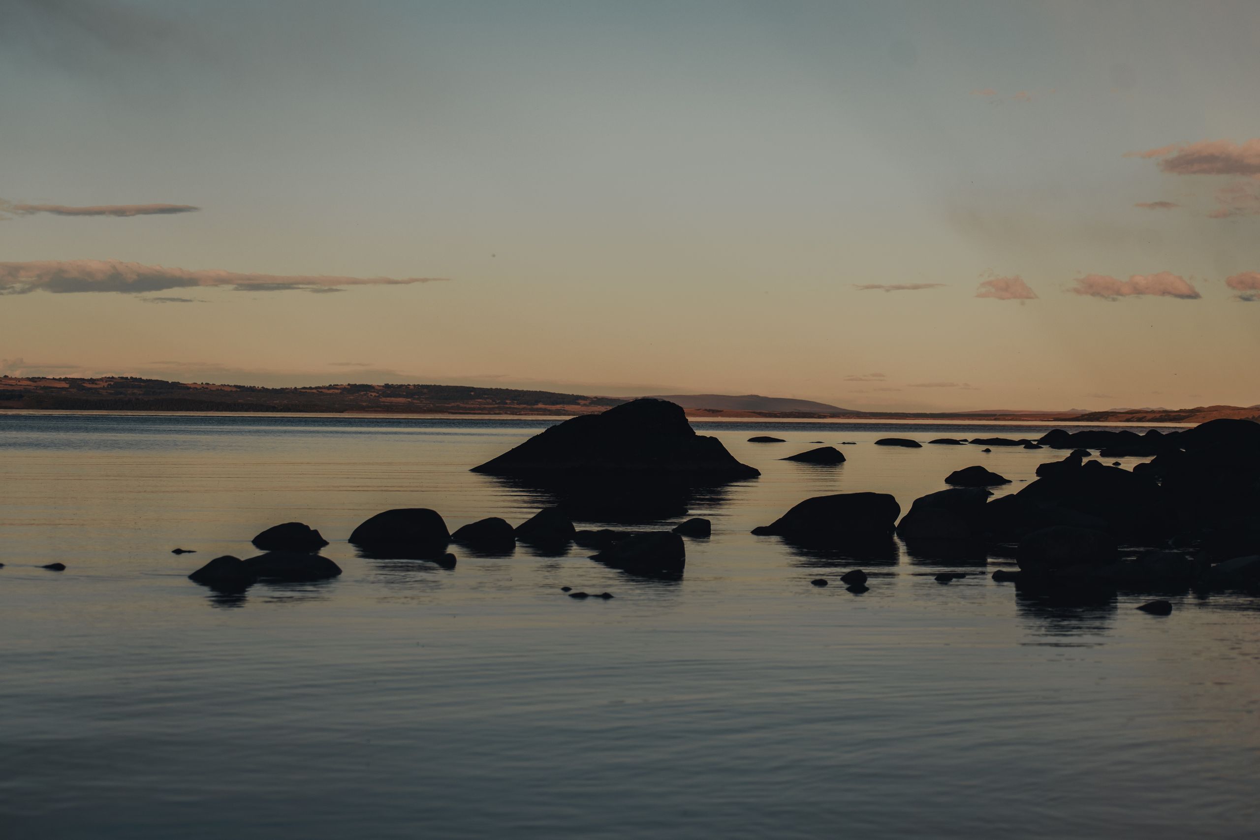 Tranquil seaside view during sunset with rocks and calm waters, ideal for nature lovers.